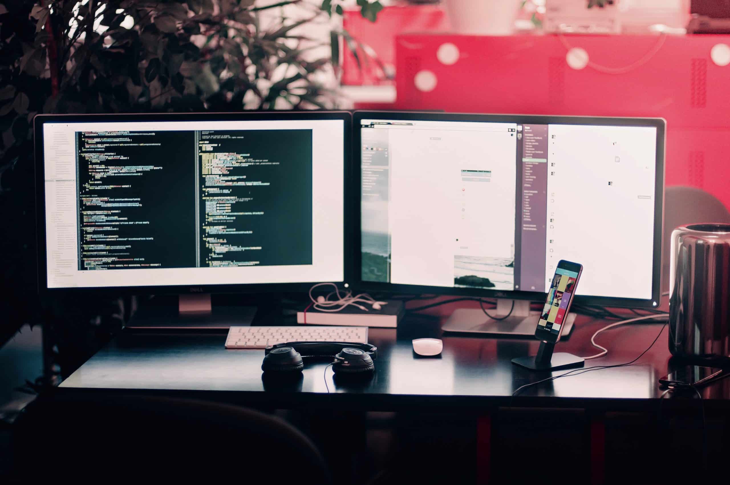  A web developers workstation with dual screens, mobile phone and headphones on the desk