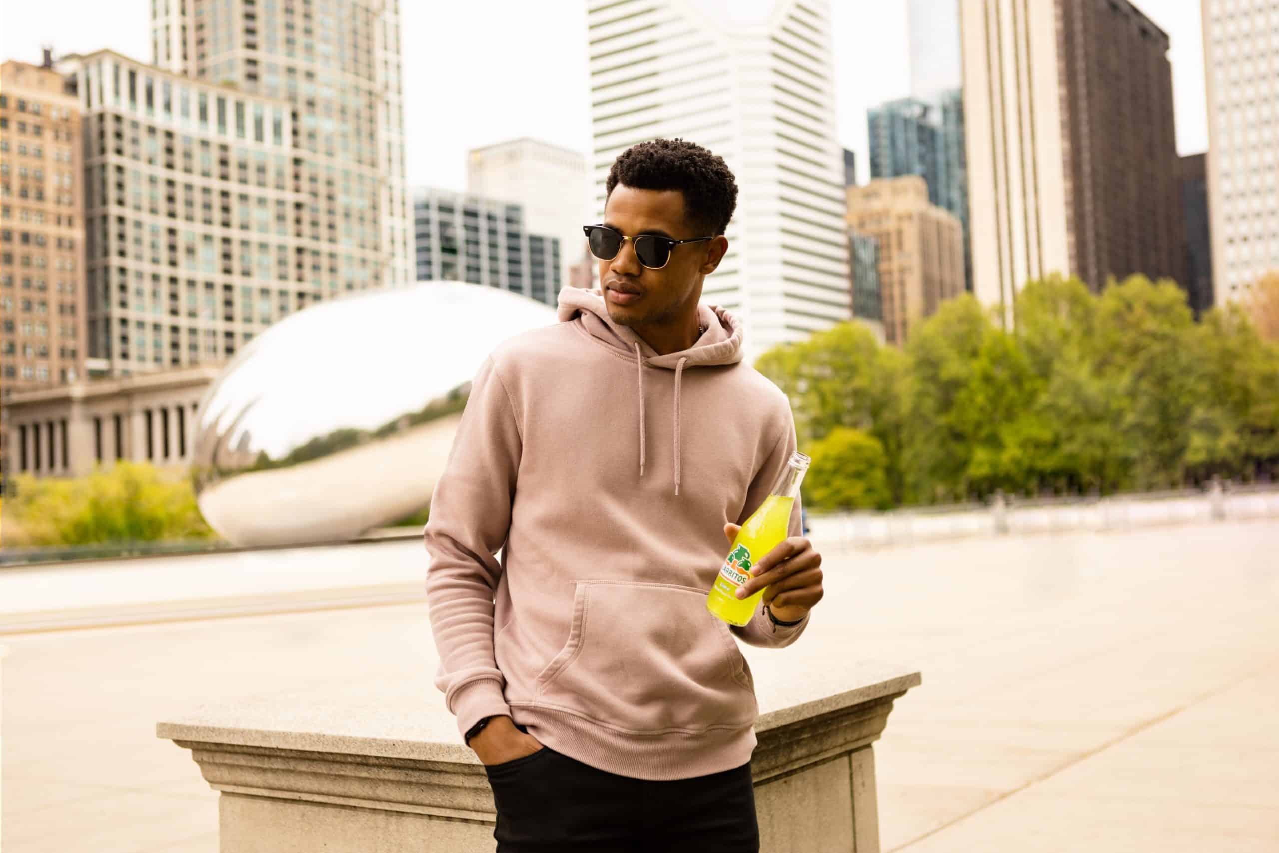  Man in sunglasses, leaning against a plinth, holding a glass bottle of soda