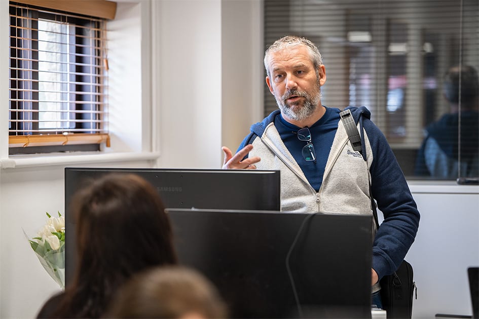 Man standing at a computer in an office with colleagues