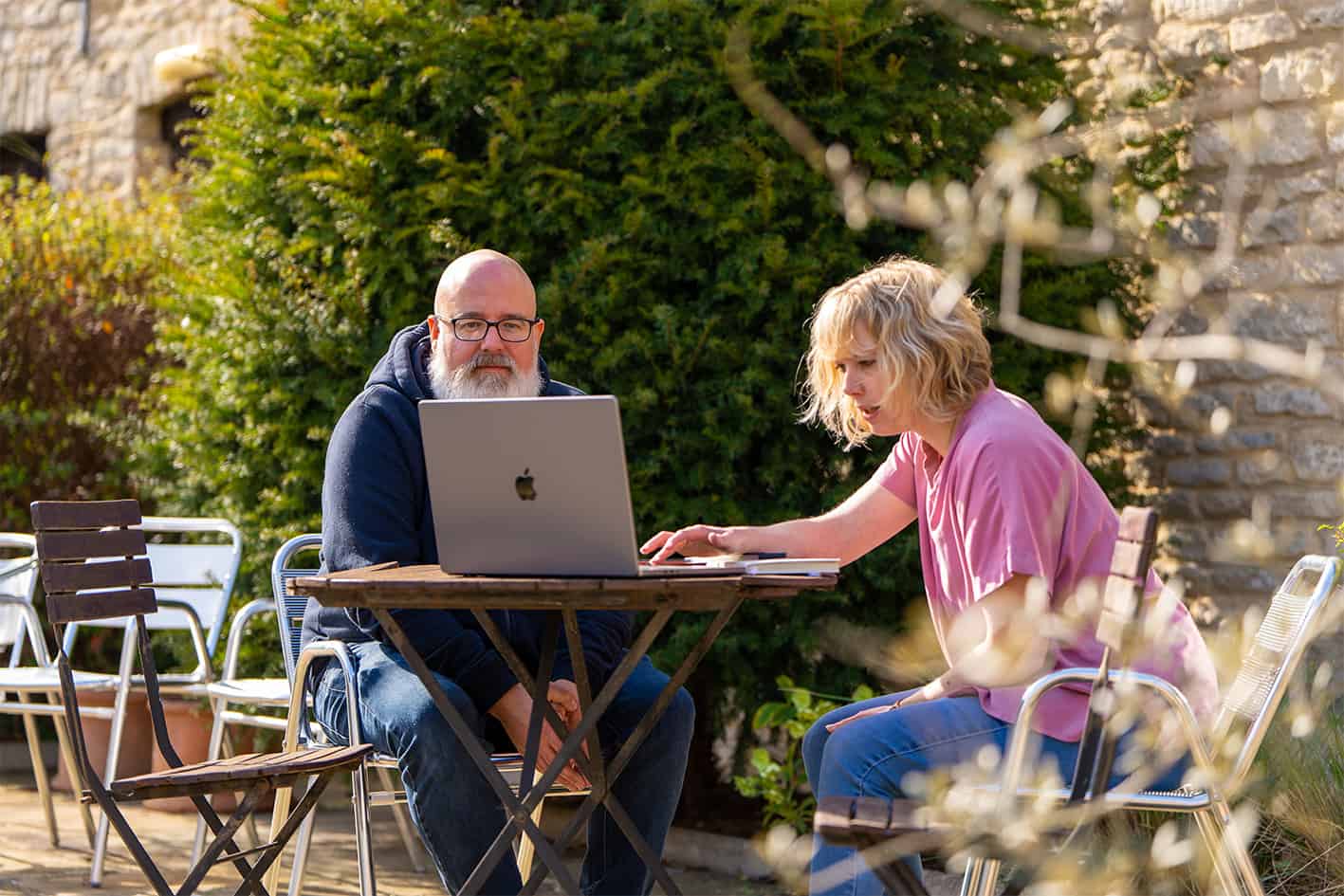 a woman and a man sat at a table outside in the sunshine